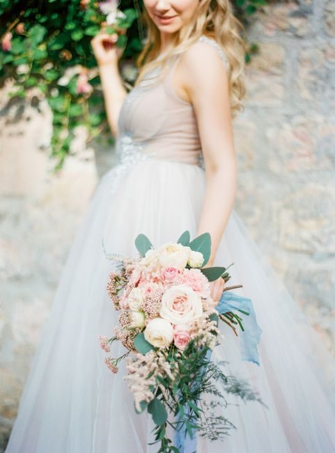 Beautiful bride holding a pastel flower bouquet in a light wedding dress outdoors.