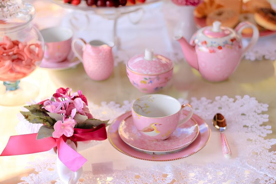 Elegant pink tea set on lace tablecloth with flowers, creating a charming afternoon tea scene.