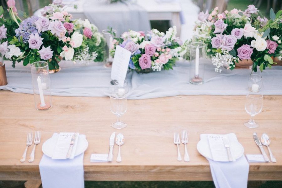 From above of wooden banquet table with plates near cutlery and decorative candles behind bright flower bouquets during festive event