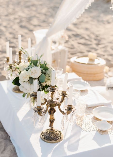An elegant beachside table setup with flowers and candle holders, perfect for a romantic occasion.