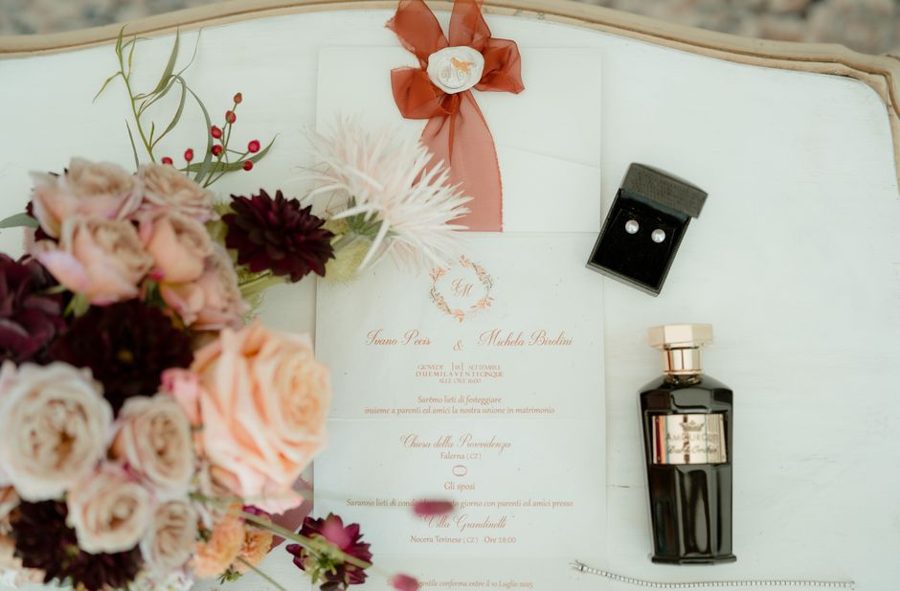 A stylish flat lay featuring a wedding invitation, flowers, perfume, and jewelry with a classic touch.