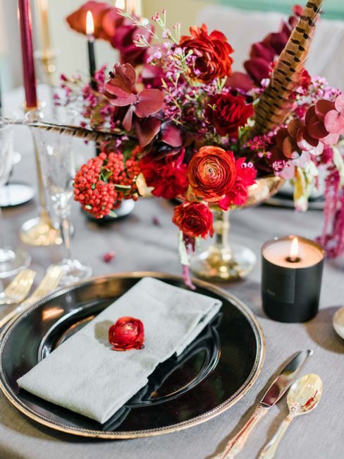 Elegant table setting with red floral centerpiece, candles, and silverware for romantic dining.