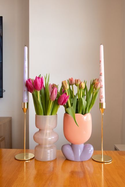 Colorful tulips in stylish vases with decorative candles on a wooden table.