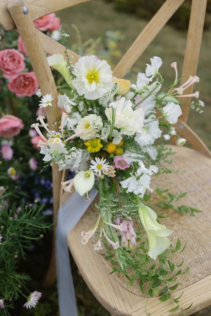 A beautifully arranged wildflower bouquet draped over a vintage wooden chair with a natural setting.