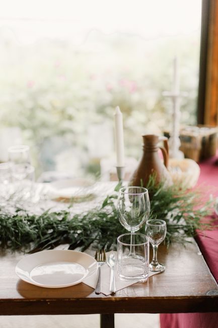Decorated table with green plant and white candles near dishware and glasses in daylight