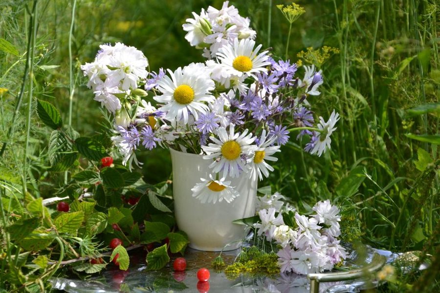 A beautiful arrangement of wildflowers in a white vase, set outdoors in lush greenery.