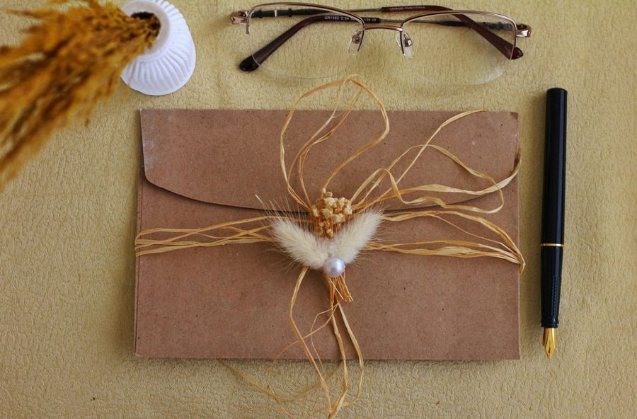 A flat lay of a decorated brown envelope with glasses and pen on a textured surface.