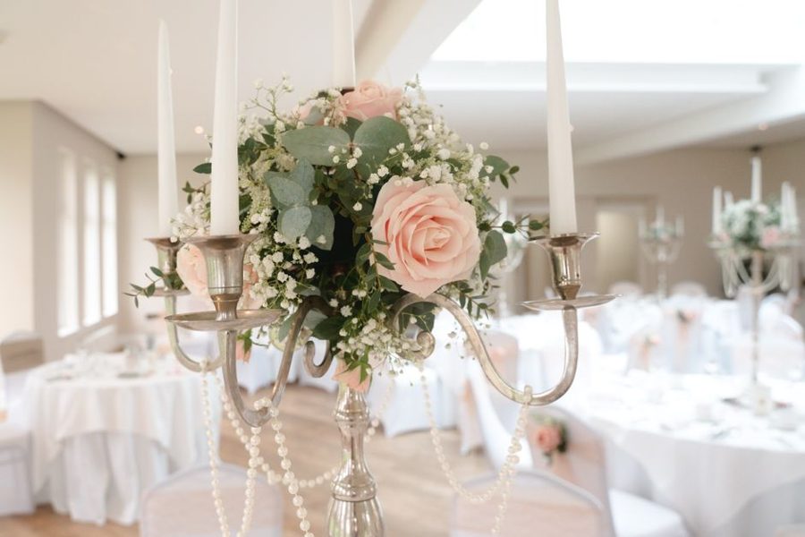 Beautiful wedding table centerpiece with pink roses and candles in a bright indoor setting.