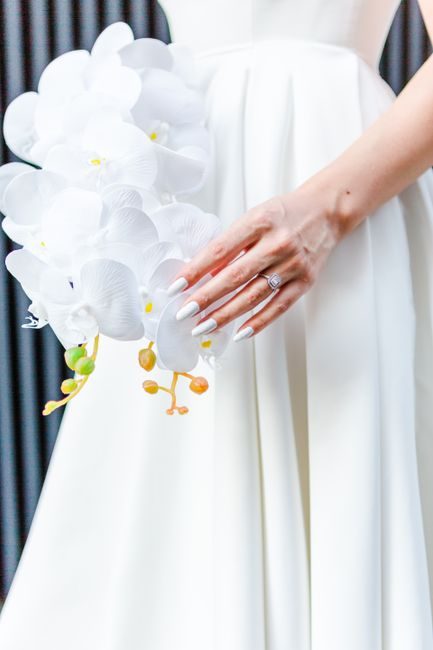 Close-up of a bride's hand holding a white orchid bouquet against her wedding dress.