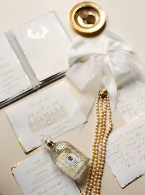 Sophisticated arrangement featuring luxury perfume, pearls, and elegant invitations.
