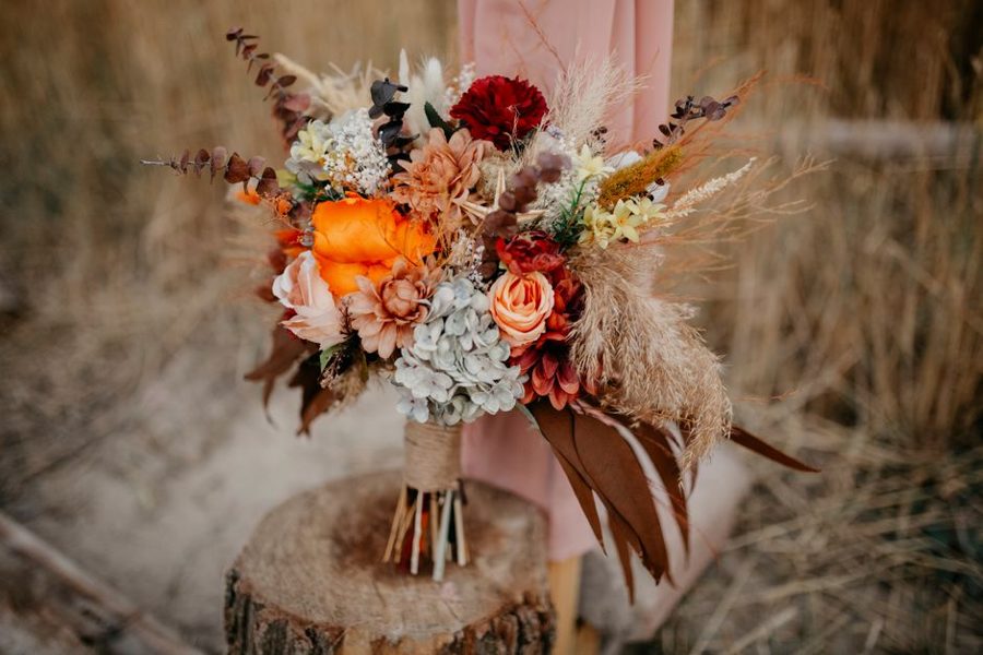 A colorful rustic bouquet resting on a tree stump, featuring a variety of flowers and leaves.