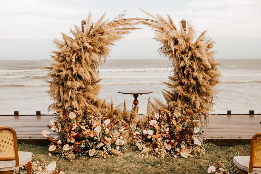 Elegant wedding ceremony setup featuring pampas grass arch by the beach.