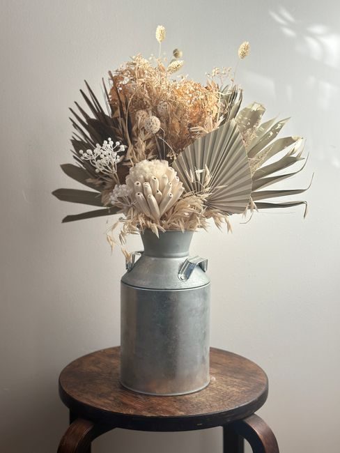 A rustic dried flower arrangement in a milk can on a wooden stool, perfect for home decor.