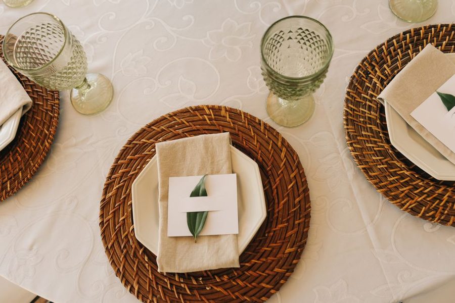 Top view of a stylish table setup featuring wicker placemats, glassware, and leaf-accented napkins.