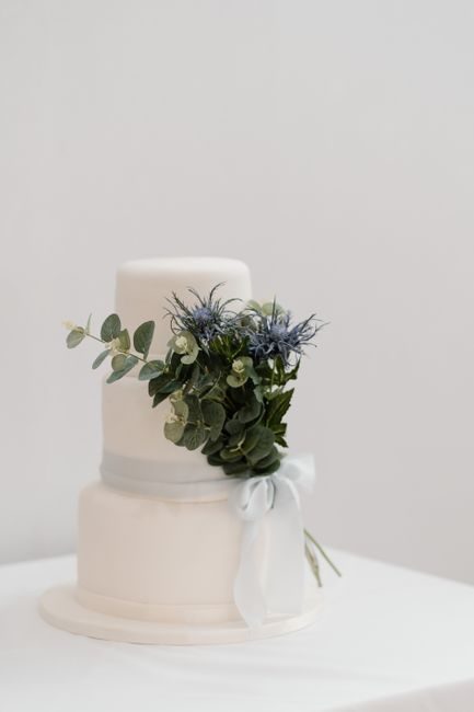 Minimalist white wedding cake adorned with eucalyptus and thistle flowers, perfect for celebrations.