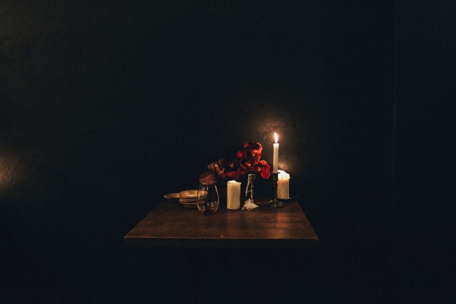 Intimate table setting with candles and red roses at night in a dark room.
